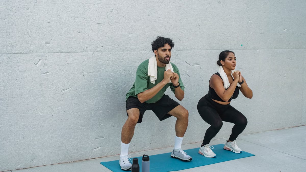Focused couple performing squats outdoors on yoga mat, showcasing teamwork and healthy lifestyle.